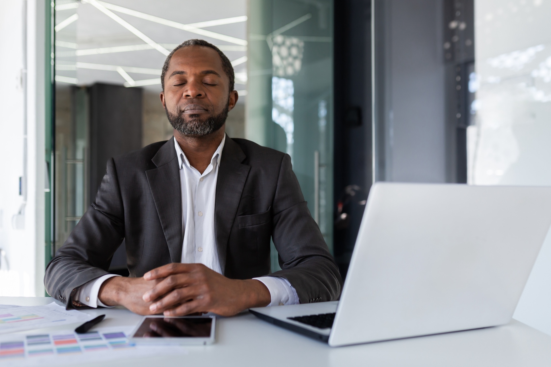 Balanced and calm man at workplace inside office, businessman meditating with closed eyes thinking and visualizing future projects and plans financial strategies, boss inside office with laptop.